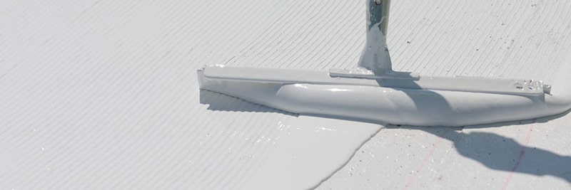 A thick, white fluid-applied roofing membrane is applied to a rooftop