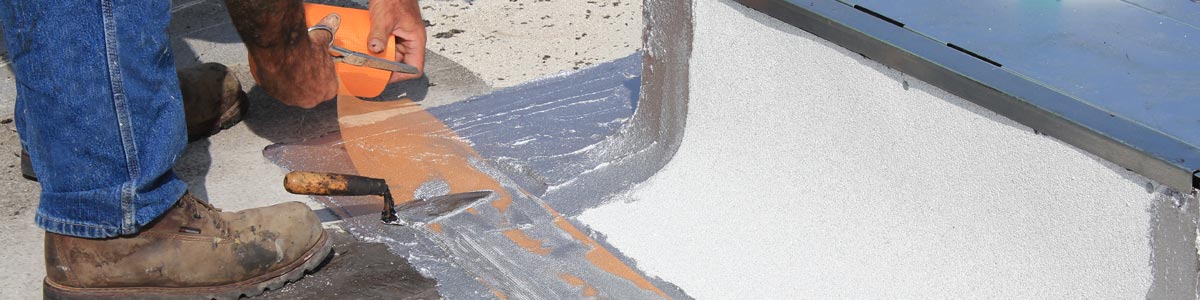 A worker cuts self-priming tape seals reinforcements on a roof.